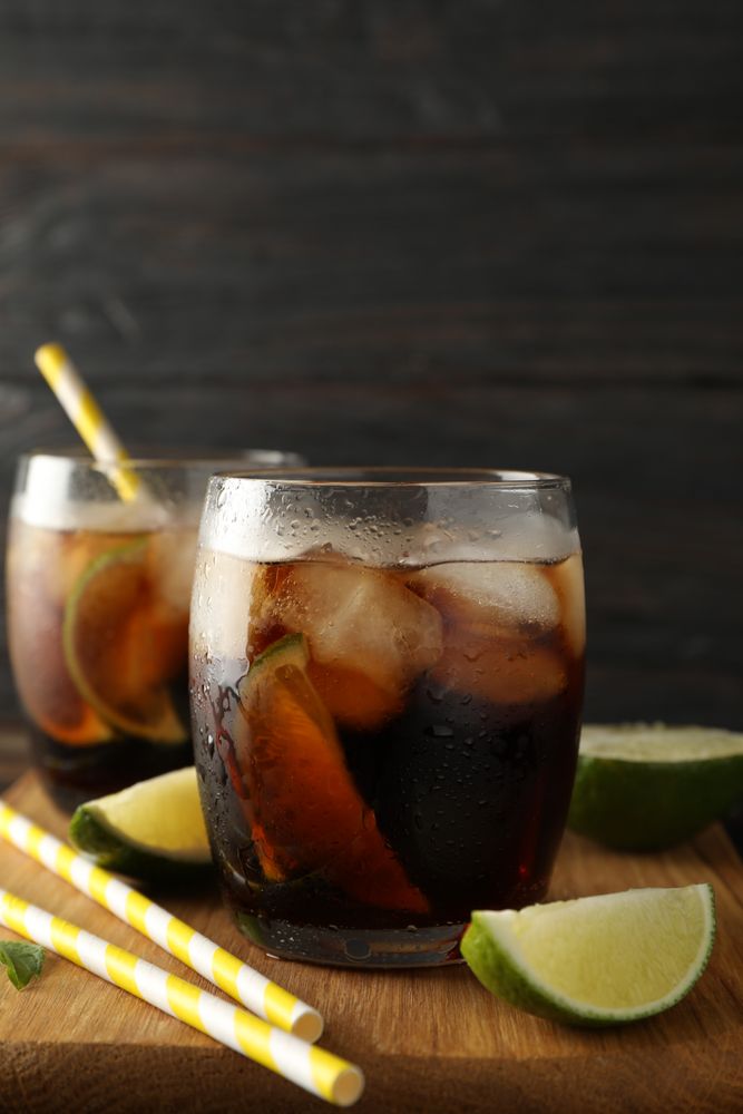 Glasses with ice cola, lime slices and tubules on wooden background