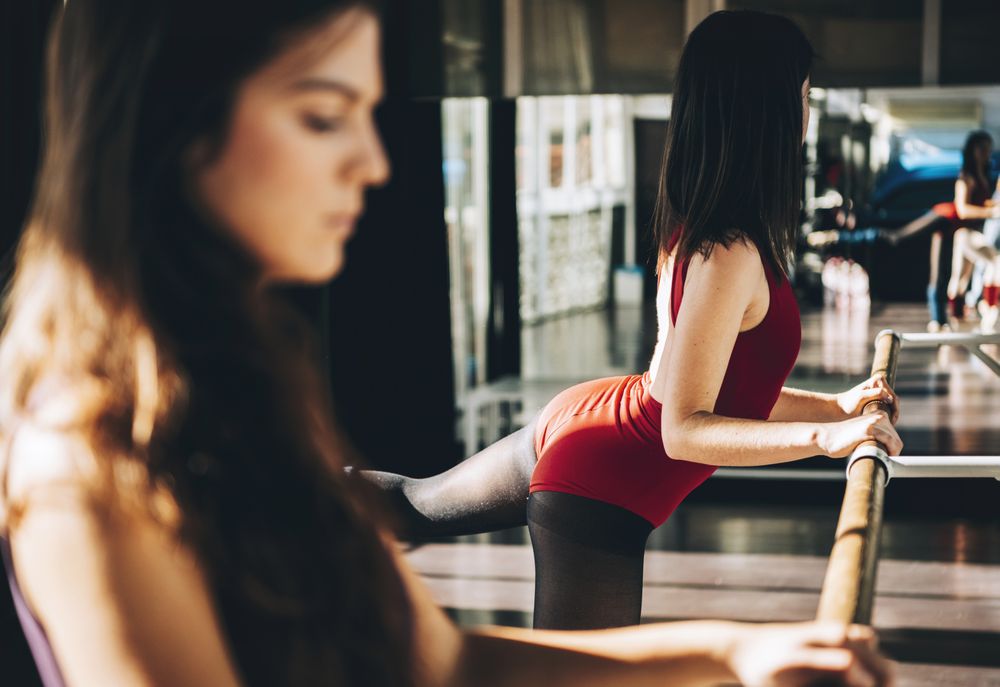 Side view of women practicing ballet with barre in sunny studio.