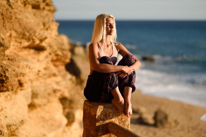 Blonde woman sitting on fence over looking beach