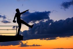 Out line of male walking off ledge and holding tablet against a colorful dusk side, vertical