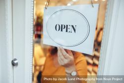 Woman hanging an open sign on the door of her store 4dGMD5