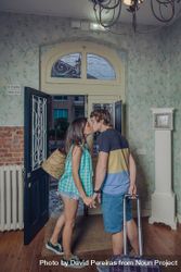 Couple kiss in entrance of home with roller suitcase 0PjNX7