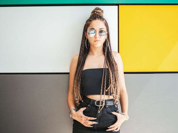 Charming teenage girl with dreadlocks in sunglasses nearby colorful wall