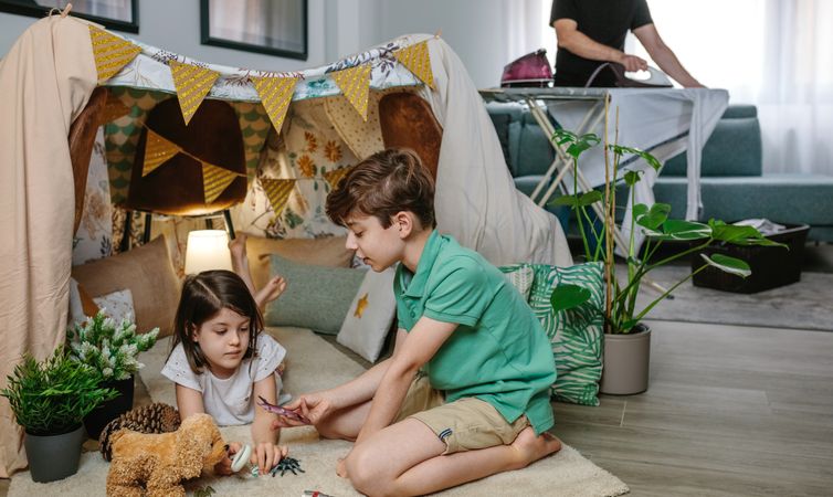 Children playing camping at home while their father irons