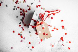 St. Valentine day concept with small gift wrapped in red ribbon and heart confetti