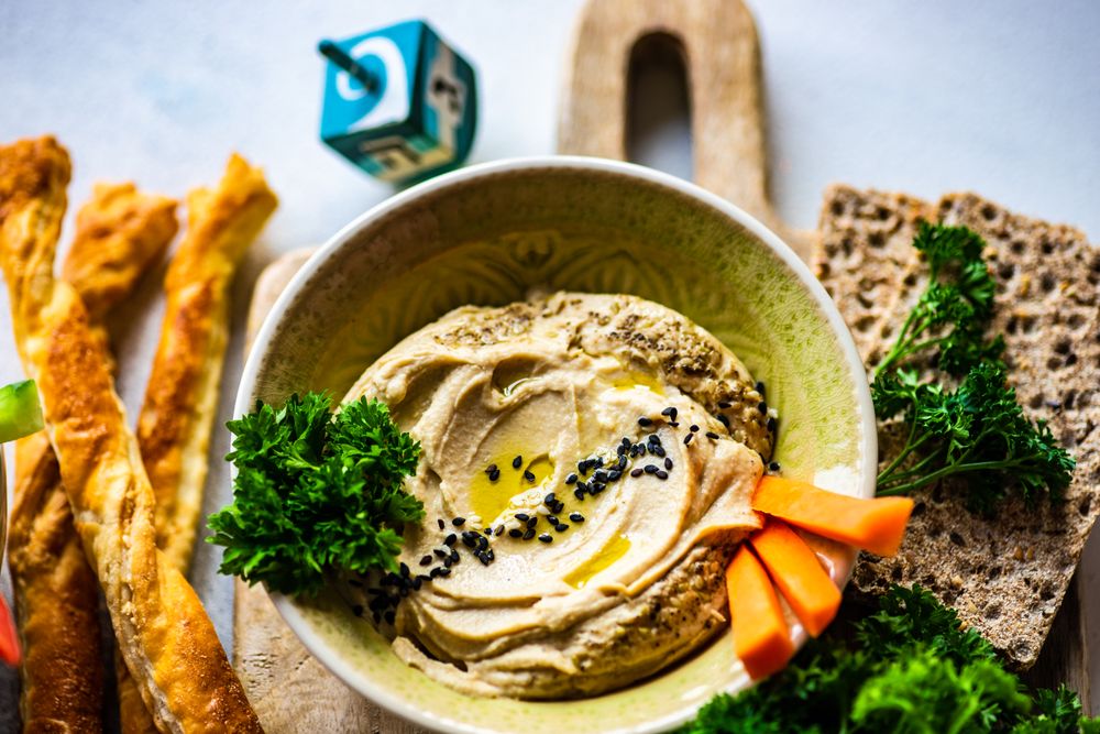 Creamy hummus dip in bowl on cutting board served with veggies and crackers