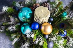 Blue and gold Christmas baubles in pine centerpiece with candle and peacock feathers