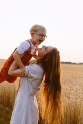 Cheerful mom holding up cute son on wheat field
