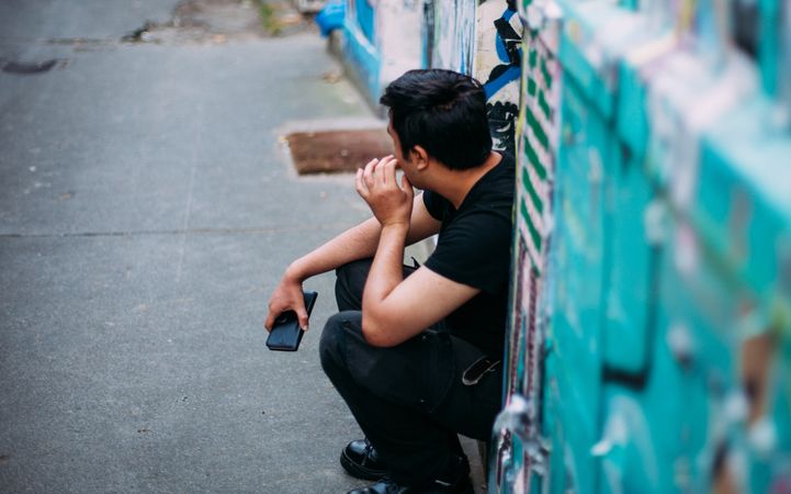 Side view of young man in casual outwear sitting on doorstep outdoor