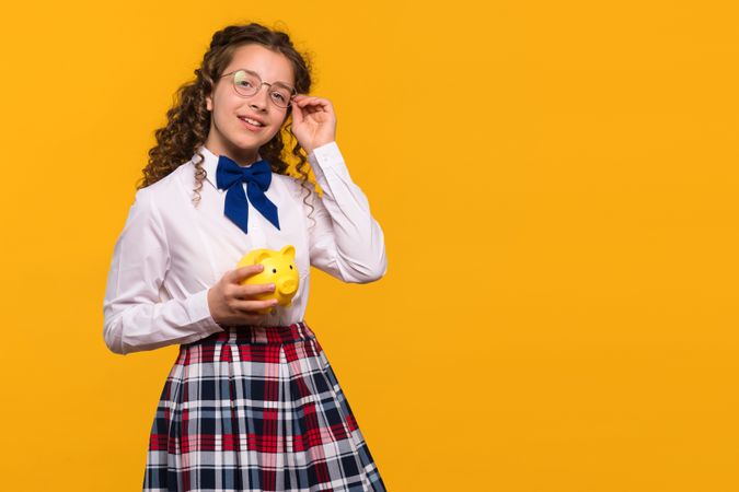 Girl in glasses holding yellow piggy bank