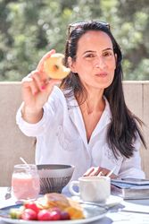 Positive woman showing bitten tasty donut while eating breakfast