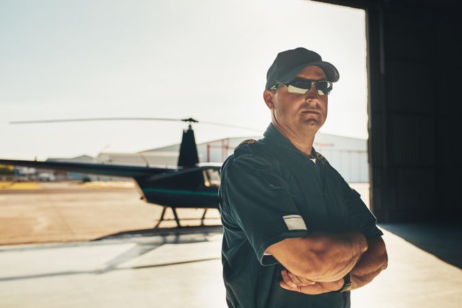 Serious man with arms crossed in front of helicopter