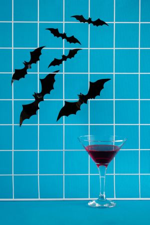 Bats flying above a cocktail glass on blue background