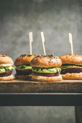 Upright fresh vegan burgers on seeded buns with skewer on wooden board