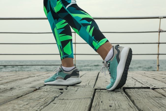 Female legs in bright leggings and sneakers on wooden floor outdoors, close up