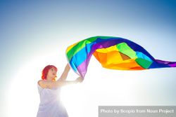 Woman waving rainbow flag under blue sky bDmmp0