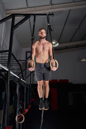 Shirtless sporty guy exercising with gymnastic rings