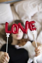 Close up shot of a red balloon that spells “love” with a woman and dog snuggling in the background