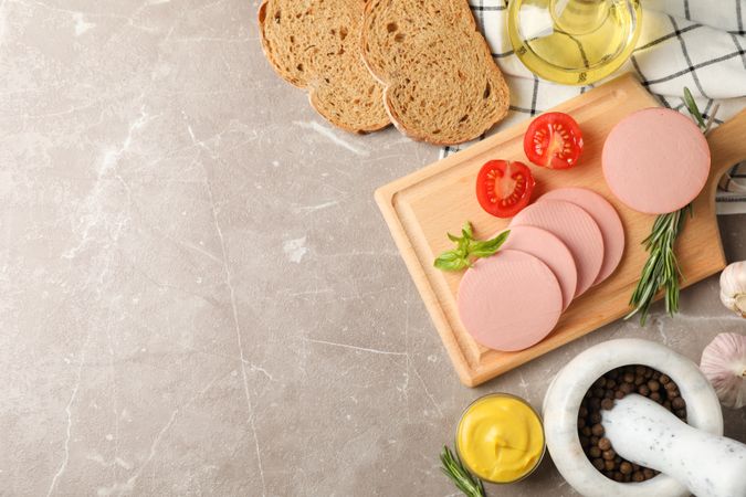 Sliced sandwich meat with bread slices, mustard and tomato, top view