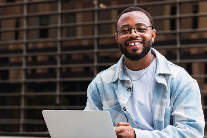 Cheerful Black man browsing laptop on street