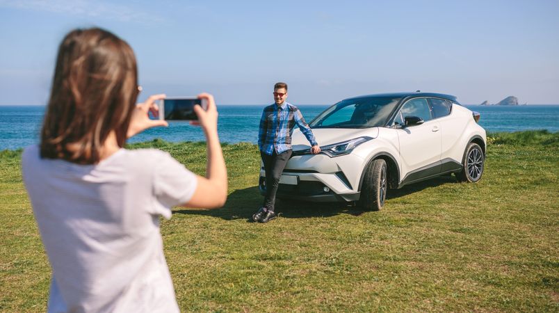 Woman taking picture of guy leaning on a car