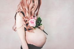 Side view of pregnant woman wearing dark bra holding pink rose bouquet