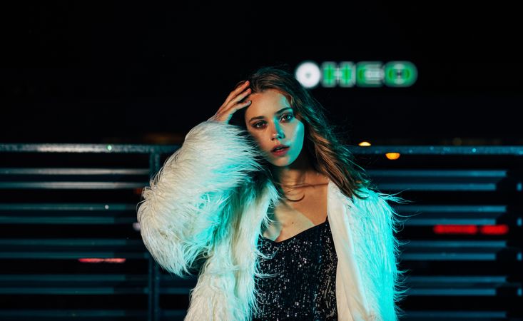 Female model in long faux fur coat posing at night on a rooftop terrace