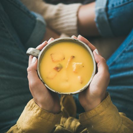Woman in jeans holding cup of squash soup, square crop