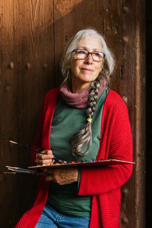 Cheerful mature painter with paint palette looking at camera