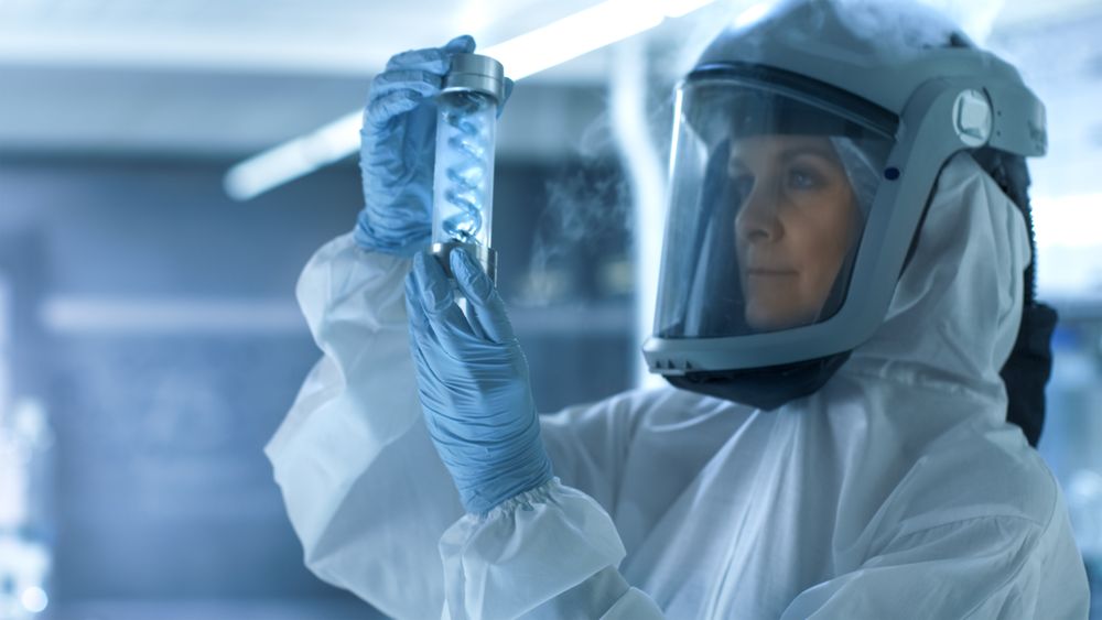 Medical Virology Research Scientist Works in a Hazmat Suit with Mask, Inspects Test Tube with Isolated Virus String from Refrigerator Box.