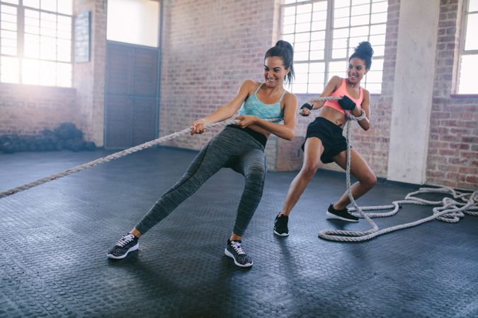 Two strong young women doing rope pulling exercises in gym