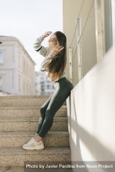 Woman leaning on wall near outdoor concrete stairs in workout clothes 5ngYn4