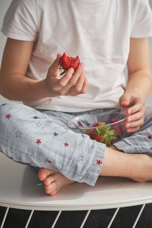 Crop child with bitten strawberry in hand