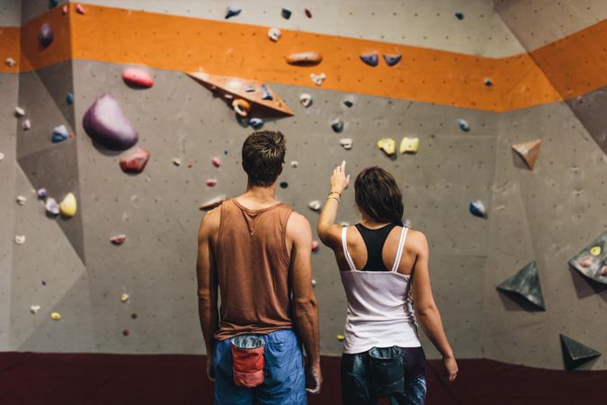 Rear view of female instructor giving instructions to man on rock climbing wall