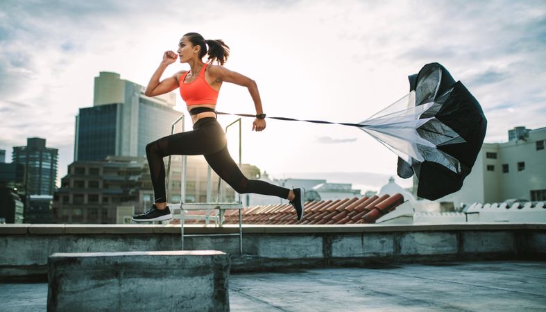 Female athlete training on terrace of a building with a parachute tied behind her