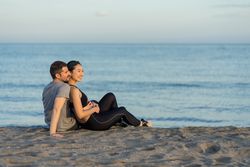 Happy couple in sportswear sitting on beach