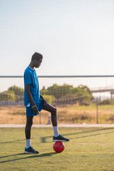 Black football player with ball standing on stadium