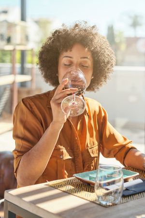 Young Black Latina female drinking red wine in sushi restaur
