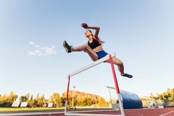 An athletic woman jumping hurdles on an athletics track.