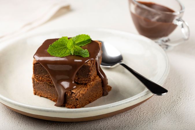Brownies with spoon served with pot of chocolate sauce and mint garnish
