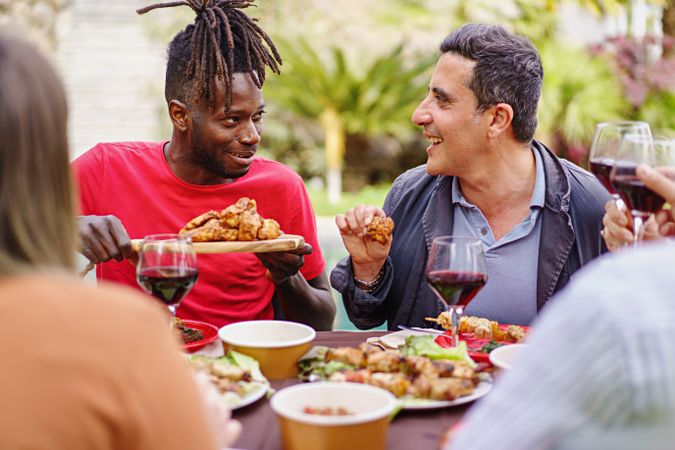 Happy multi-ethnic friends sitting at farmhouse table sharing a plate of chicken