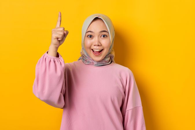 Excited Muslim woman smiling and pointing upwards with good idea