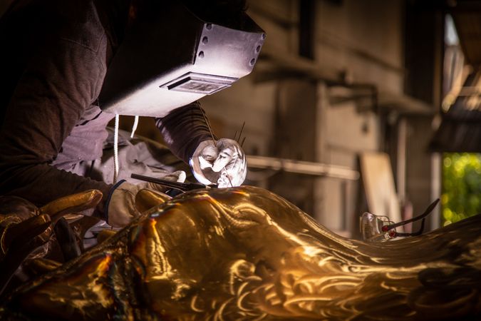 Man in mask welding metal ware in darkness