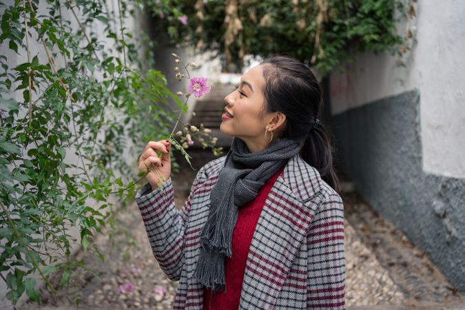 Young female in casual clothing touching green plants and smiling at rocked lane