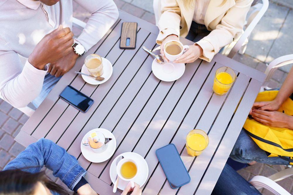 Looking down at hands of people with coffee and juice at outdoor table