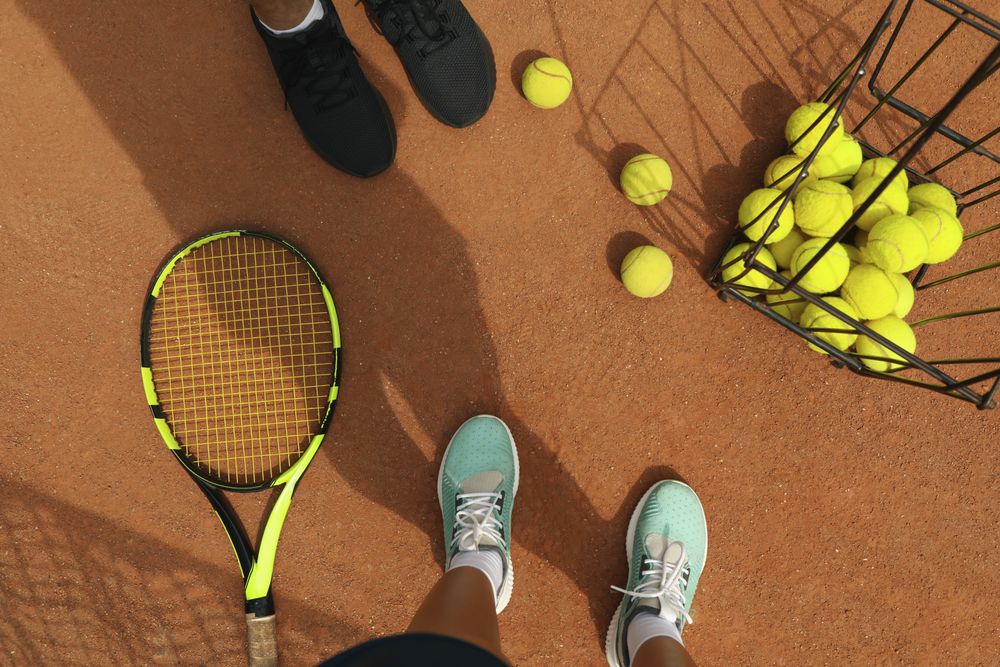 Woman and man legs in sneakers on clay court with tennis balls and racket