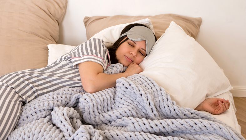 Woman sleeping peacefully in bed wearing eye mask.