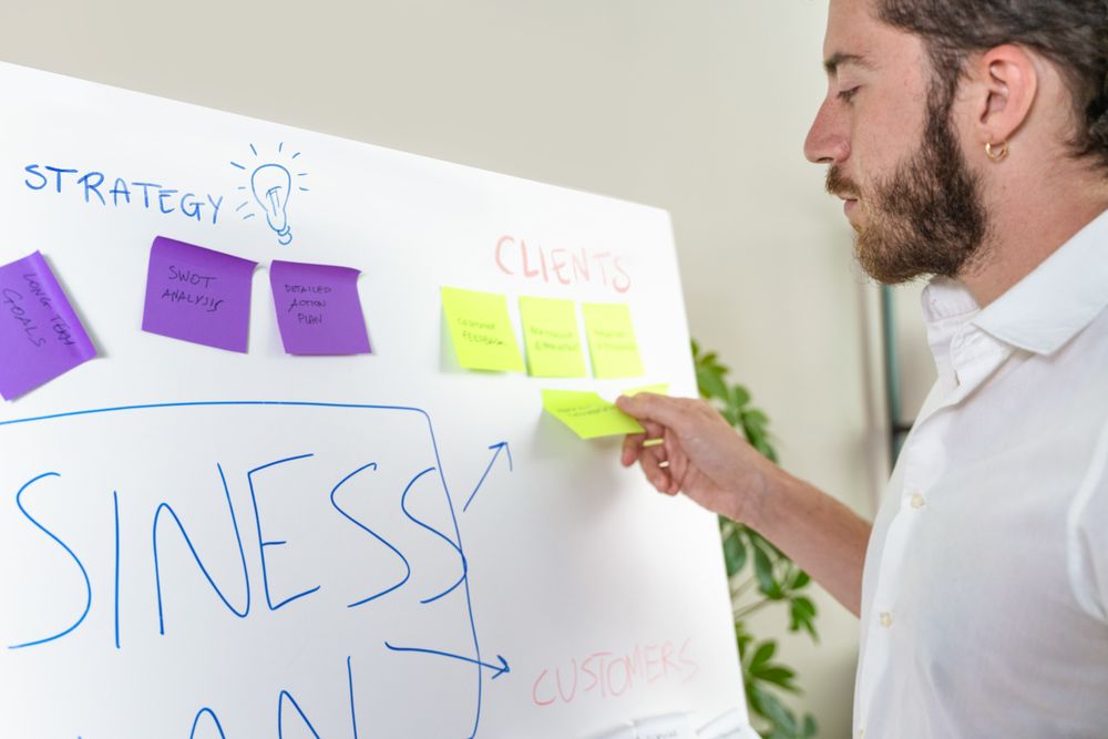 Young man planning a business strategy on a whiteboard with sticky notes.Young man planning a business strategy on a whiteboard with sticky notes.