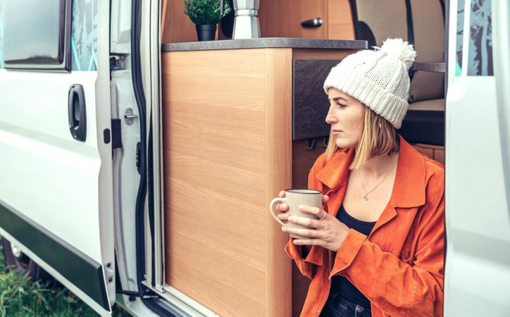 Female relaxing with coffee sitting on camper van step, close up
