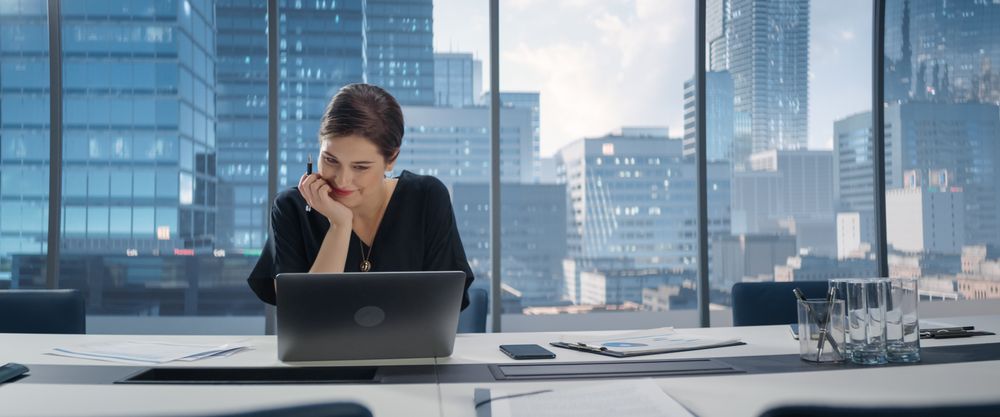 Portrait of Successful Young Businesswoman Sitting at Her Desk Working on Laptop Computer in Big City Office.